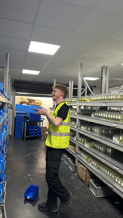 Person in a warehouse with shelves and storage units containing perfume bottles.